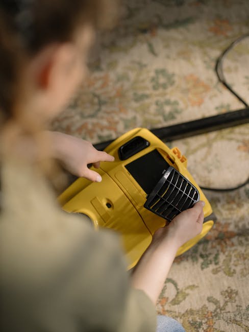 A person operating a yellow portable fan or air scrubber on a patterned carpet in a room with wooden flooring. The individual is holding the device with both hands, focusing on the surface cleaning process for deep cleaning or sanitisation as part of a domestic cleaning service. The carpet features a traditional floral or oriental design in muted tones, and the room is softly lit, emphasizing cleanliness and hygiene. The scene highlights professional cleaning routines offered by Streatham Cleaners in their residential carpet cleaning service, maintaining high standards of surface cleanliness and hygiene.