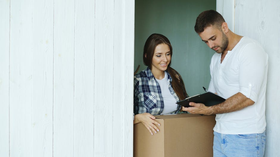 A professional cleaner from Streatham Cleaners is conducting a surface inspection during an end of tenancy cleaning process in a residential property. The cleaner, dressed in a casual white shirt, is holding a clipboard or checklist and reviewing details with a female tenant who is standing behind a cardboard moving box. The room features white-painted wooden walls, and soft natural lighting highlights the clean, tidy environment. The focus is on the thorough assessment of surfaces, ensuring hygiene and cleanliness for a smooth move-out process as part of comprehensive domestic cleaning services. The scene emphasizes attention to detail in surface cleaning and sanitisation in readiness for property handover, aligned with the Streatham Hill end of tenancy cleaning checklist.